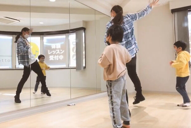 ダンスの女性講師が大きな鏡の前で子ども2人にダンスを教えている写真