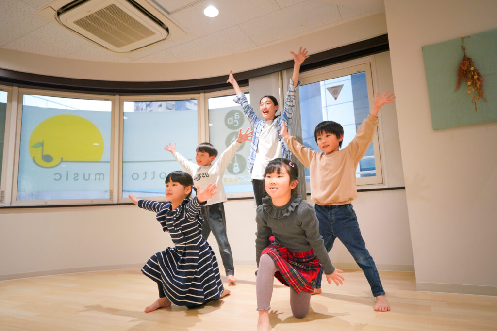 ダンスの女性講師が大きな鏡の前で子ども4人にダンスを教えている写真
